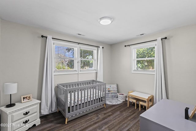 bedroom with dark wood finished floors, a nursery area, multiple windows, and visible vents