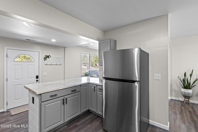 kitchen with a peninsula, dark wood-style floors, freestanding refrigerator, and gray cabinetry