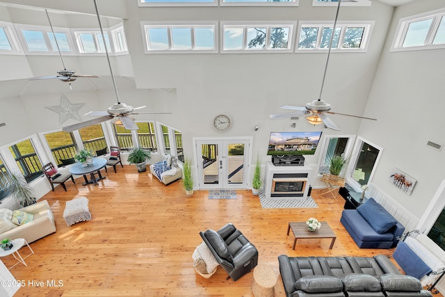 living area featuring wood finished floors, visible vents, a high ceiling, french doors, and a glass covered fireplace