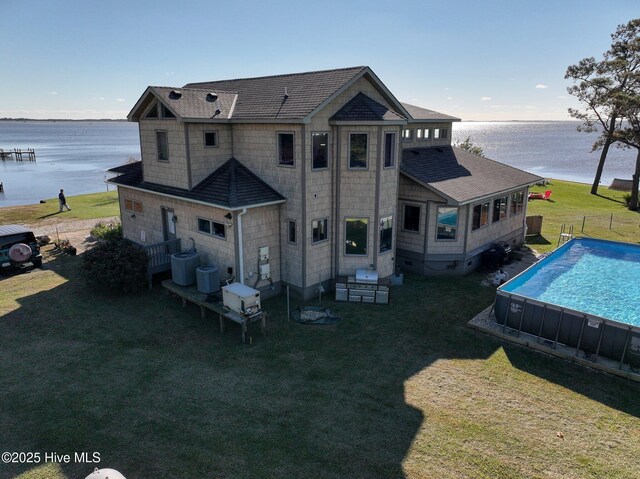 rear view of property with a fenced in pool, a water view, a lawn, and roof with shingles