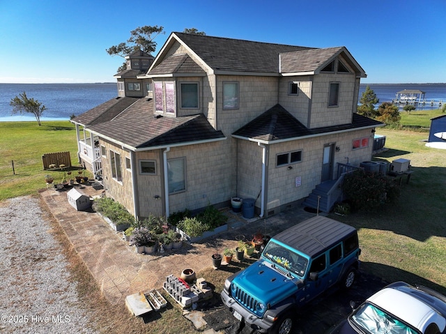 exterior space with a front yard, roof with shingles, and a water view