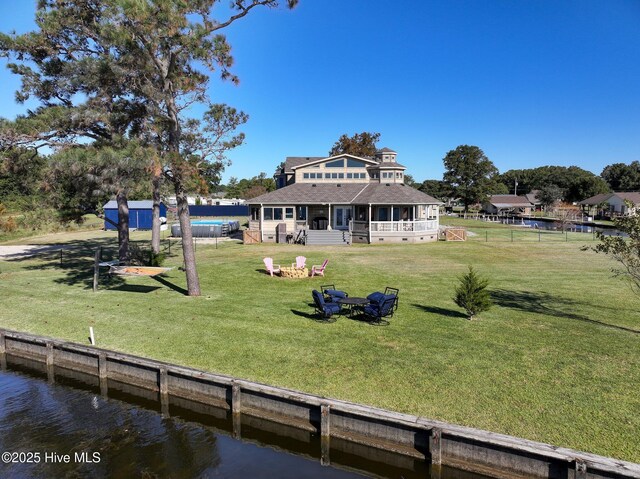 back of property featuring fence, an outdoor fire pit, a yard, a swimming pool, and a water view