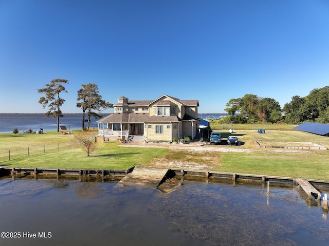 rear view of house featuring a lawn, an outdoor pool, fence, and a water view