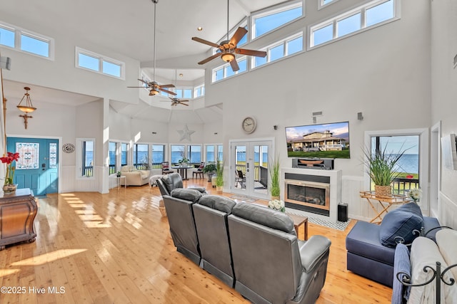 living room with a ceiling fan, a wainscoted wall, light wood-style flooring, french doors, and a glass covered fireplace