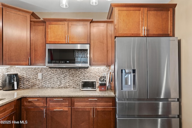 kitchen with brown cabinets, light stone counters, tasteful backsplash, and stainless steel appliances