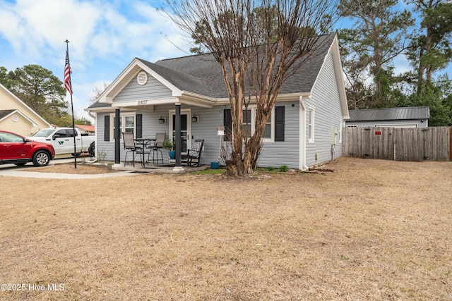 view of front facade featuring covered porch, a shingled roof, a front yard, and fence