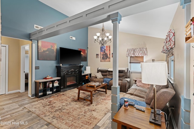 living room featuring visible vents, lofted ceiling, wood finished floors, a notable chandelier, and a glass covered fireplace