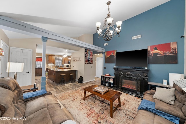 living area with visible vents, light wood finished floors, lofted ceiling, a glass covered fireplace, and a notable chandelier