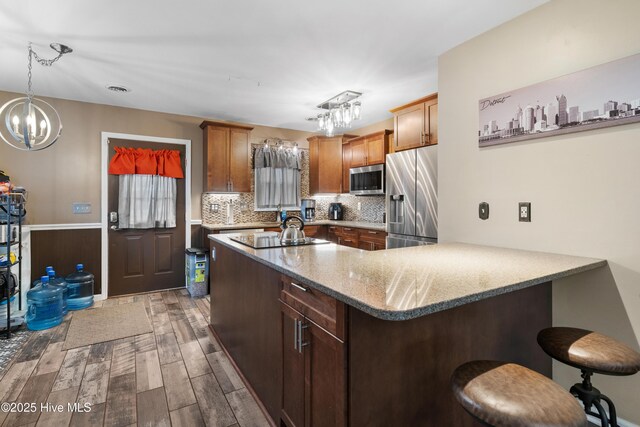 kitchen featuring wood finished floors, an inviting chandelier, stainless steel appliances, a kitchen bar, and tasteful backsplash