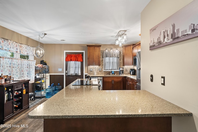 kitchen featuring a sink, decorative backsplash, an inviting chandelier, and a peninsula