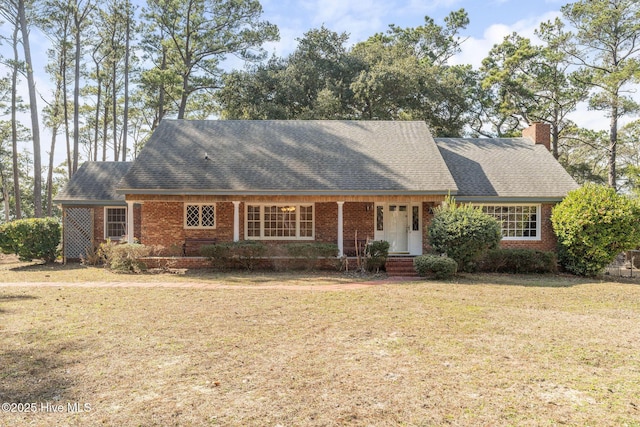 view of front of home featuring brick siding, a chimney, a front lawn, and a shingled roof