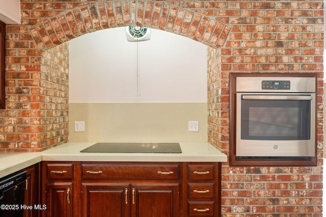 kitchen featuring black appliances, brick wall, and light countertops