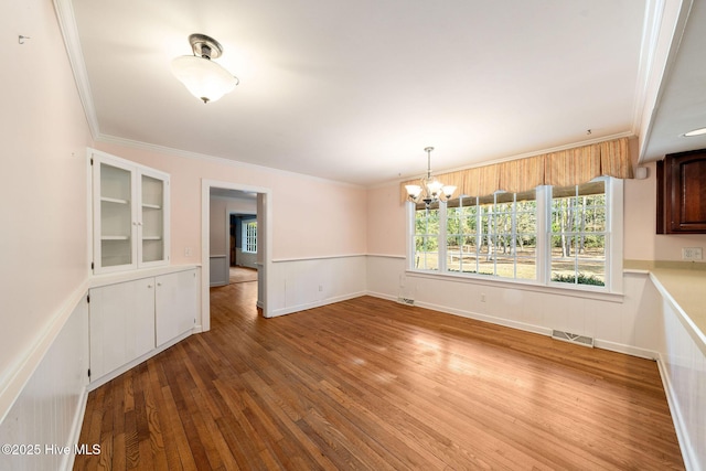 unfurnished dining area featuring visible vents, wood-type flooring, and ornamental molding