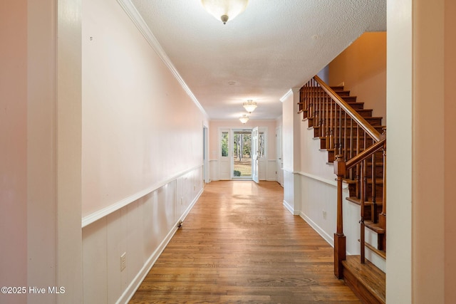 corridor featuring a wainscoted wall, a textured ceiling, wood finished floors, and crown molding