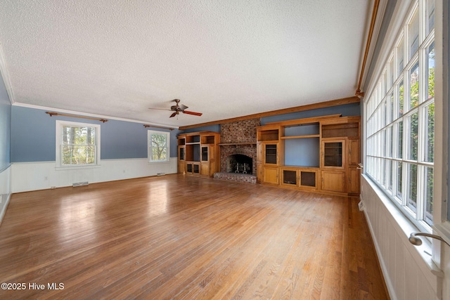 unfurnished living room with a wainscoted wall, visible vents, light wood-style flooring, a textured ceiling, and a fireplace