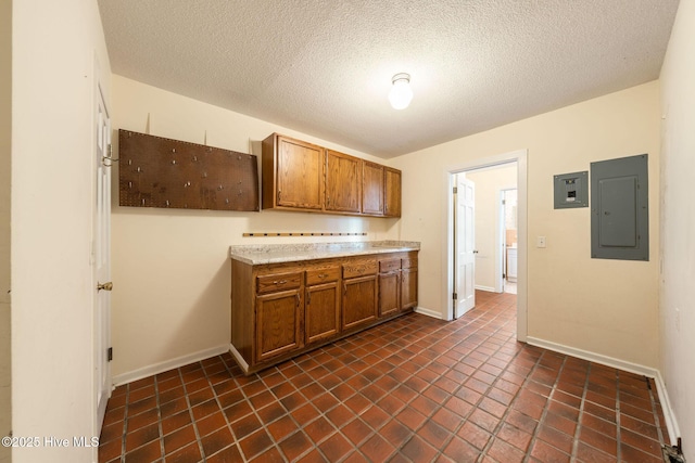 kitchen featuring baseboards, light countertops, electric panel, brown cabinetry, and a textured ceiling