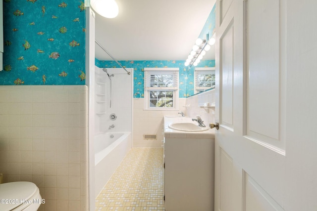 bathroom featuring vanity, wallpapered walls, wainscoting, tile walls, and toilet