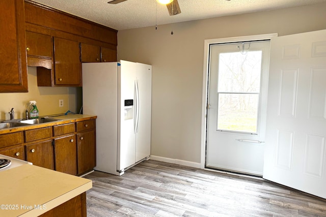 kitchen featuring light wood finished floors, ceiling fan, a sink, white fridge with ice dispenser, and a textured ceiling