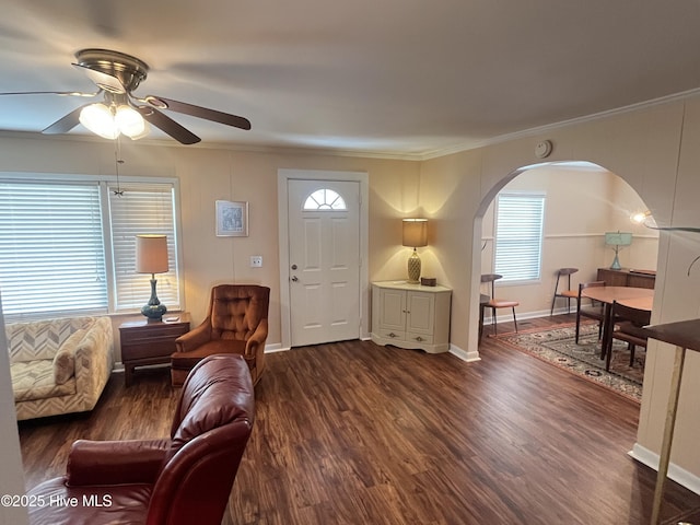 living room featuring dark wood-type flooring, ornamental molding, arched walkways, baseboards, and ceiling fan