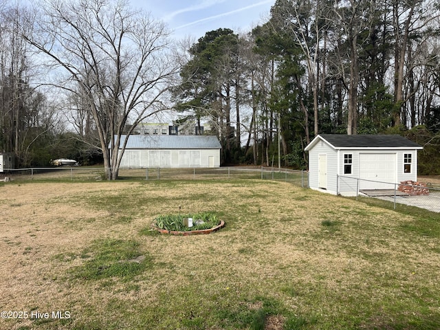 view of yard with a garage, an outdoor structure, driveway, and fence