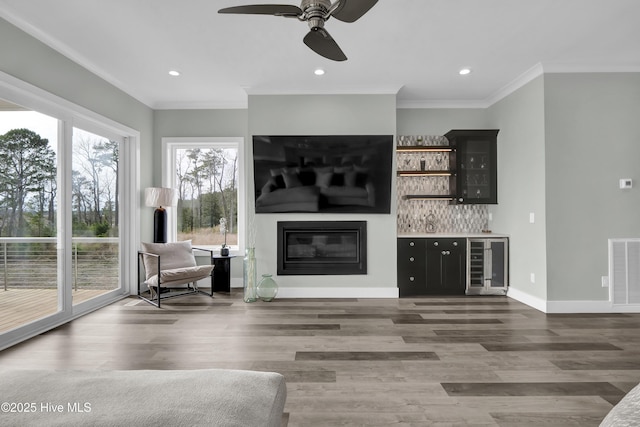 living room with visible vents, beverage cooler, a glass covered fireplace, a bar, and a ceiling fan