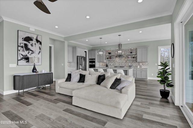 living room featuring recessed lighting, ceiling fan with notable chandelier, ornamental molding, and light wood finished floors