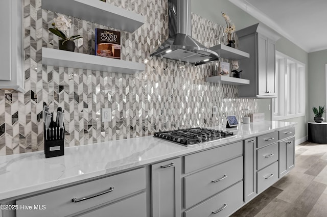 kitchen with light stone counters, open shelves, decorative backsplash, stainless steel gas stovetop, and wall chimney range hood