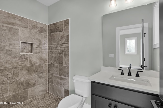 full bathroom featuring a tile shower, toilet, and vanity