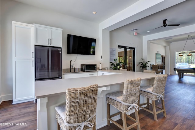 kitchen featuring dark wood finished floors, a kitchen bar, appliances with stainless steel finishes, white cabinets, and a sink