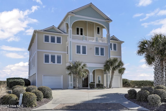 coastal home featuring a balcony, concrete driveway, and an attached garage