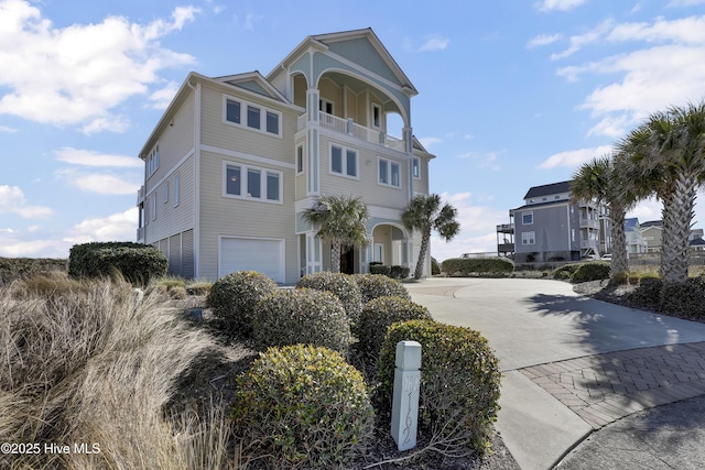 coastal home with driveway, an attached garage, and a balcony