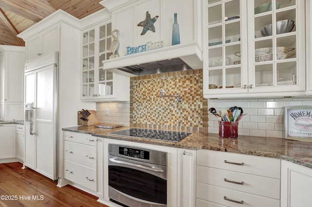 kitchen featuring paneled fridge, premium range hood, white cabinets, stainless steel oven, and black electric cooktop