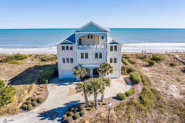 view of front facade featuring a view of the beach, a balcony, concrete driveway, a garage, and a water view