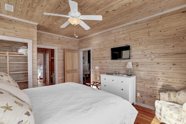 bedroom with visible vents, wood finished floors, wooden walls, wood ceiling, and ceiling fan