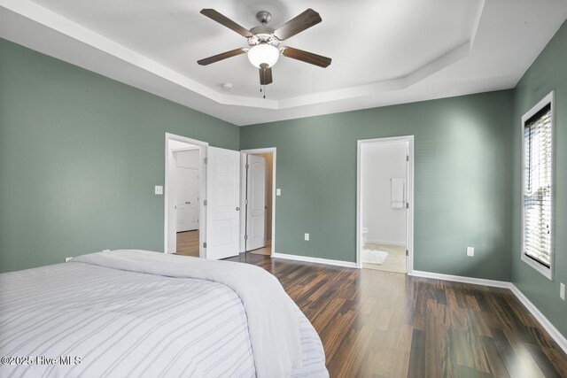 bedroom with a tray ceiling, wood finished floors, visible vents, and baseboards