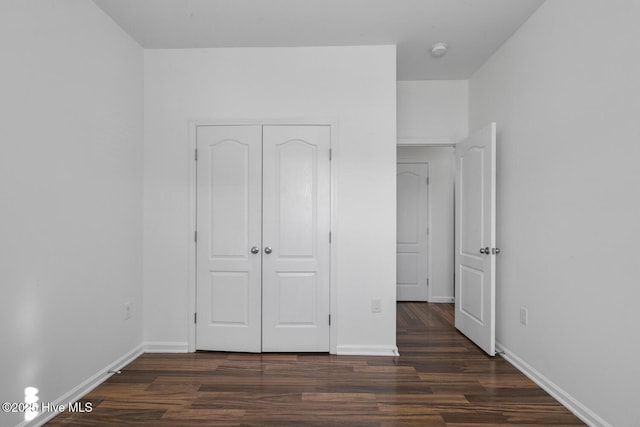 unfurnished bedroom with dark wood-style floors, baseboards, and a closet