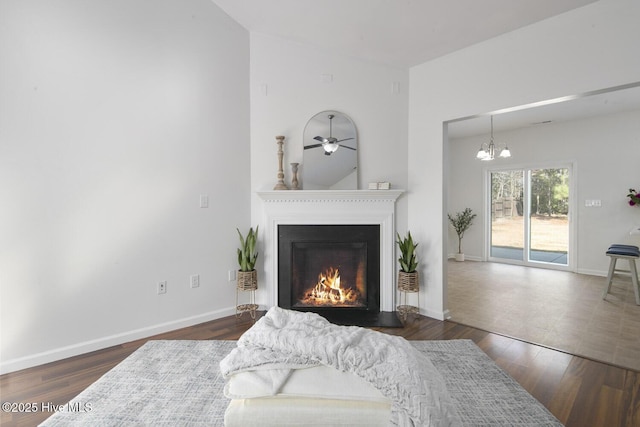 living area featuring a notable chandelier, wood finished floors, baseboards, and a warm lit fireplace