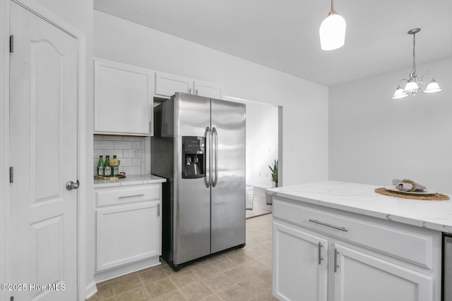 kitchen featuring light stone countertops, decorative backsplash, pendant lighting, white cabinetry, and stainless steel fridge