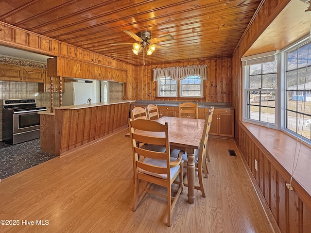 dining space with wooden walls, visible vents, ceiling fan, light wood-type flooring, and wooden ceiling