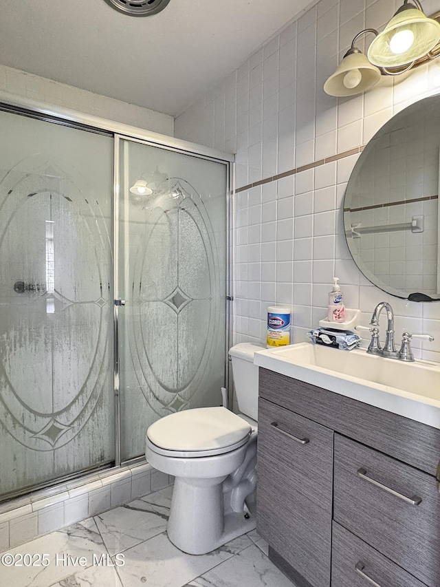 bathroom with toilet, marble finish floor, a stall shower, tile walls, and vanity