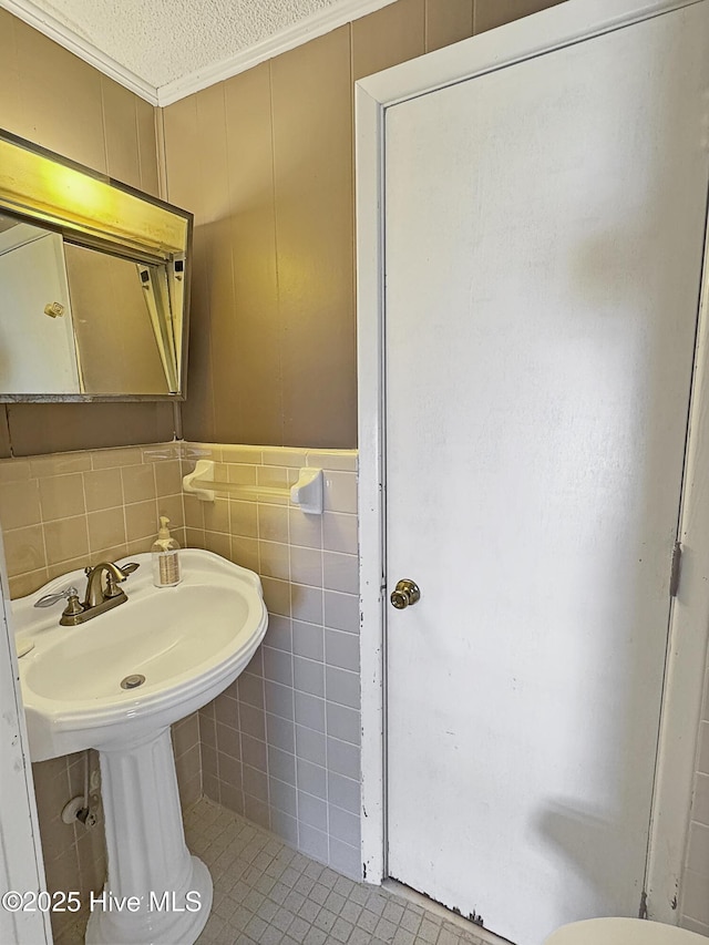 bathroom featuring a textured ceiling, tile walls, and ornamental molding