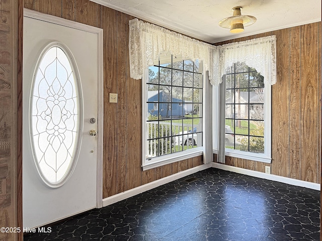 foyer with tile patterned floors, wood walls, crown molding, and baseboards