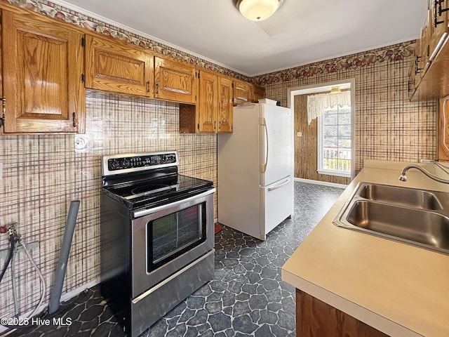 kitchen with electric range, a sink, freestanding refrigerator, brown cabinetry, and light countertops