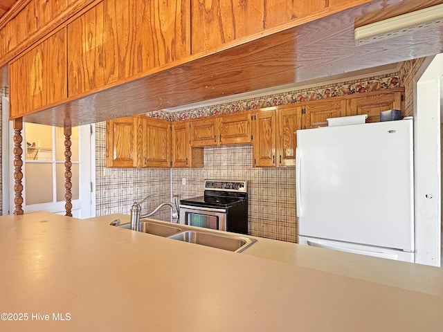 kitchen with brown cabinets, a sink, freestanding refrigerator, light countertops, and stainless steel electric range oven