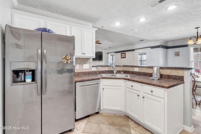 kitchen with a peninsula, a sink, stainless steel appliances, white cabinetry, and tasteful backsplash