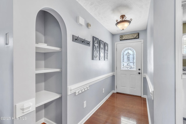 doorway with baseboards, a textured ceiling, and wood finished floors