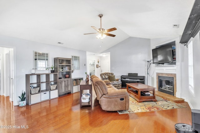 living room featuring visible vents, lofted ceiling, wood finished floors, a glass covered fireplace, and a ceiling fan