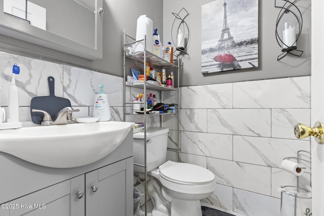 half bathroom featuring vanity, tile walls, toilet, and a wainscoted wall