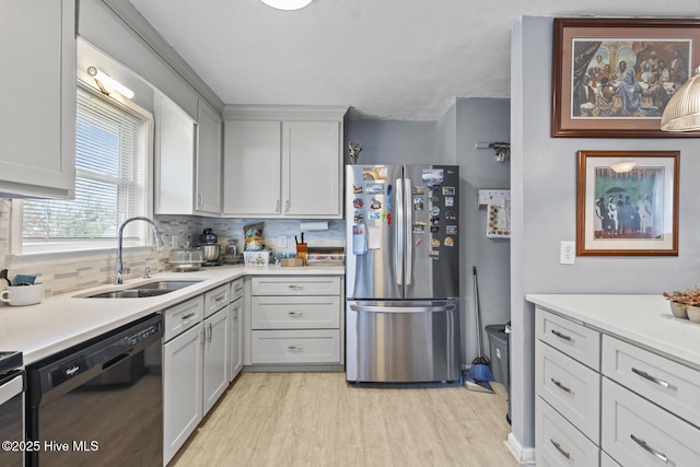 kitchen featuring light wood finished floors, light countertops, black dishwasher, freestanding refrigerator, and a sink