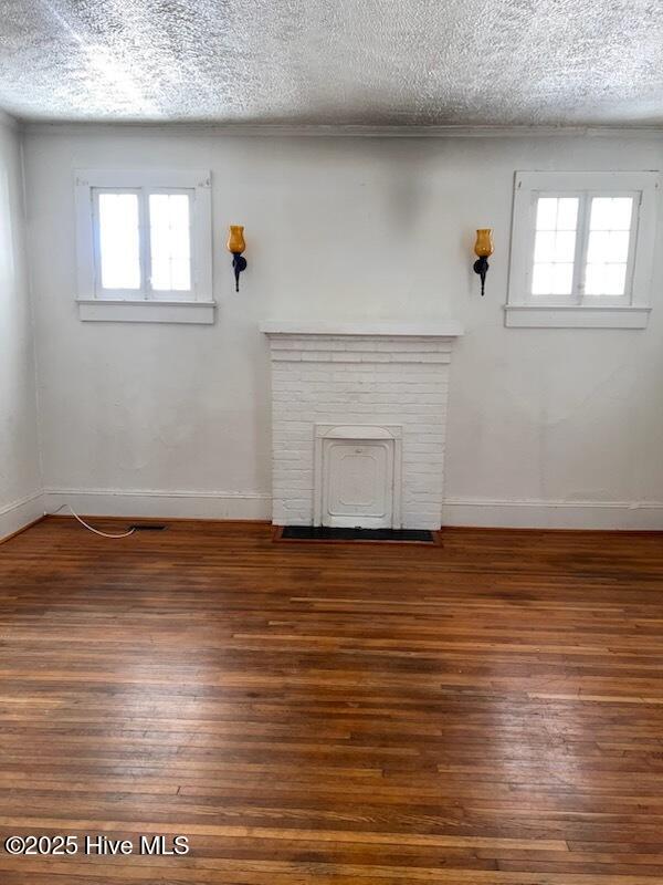 unfurnished living room with a wealth of natural light, a textured ceiling, and wood finished floors